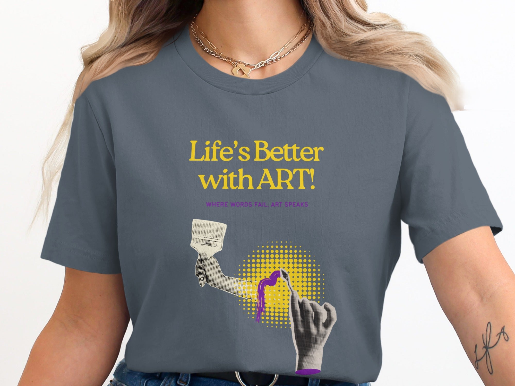 Woman in gray t-shirt with "Life's Better with ART!" text and a painted hand graphic.